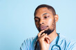 © DC Studio - Male medical assistant acting pensive against blue background, thinking about treatment and dosage to cure a patient. Young nurse pondering decision to provide a solution in studio.