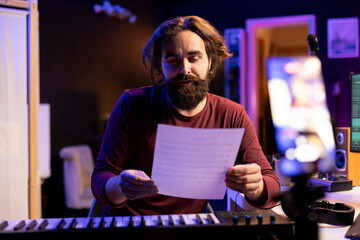 Poster - Skilled songwriter explaining music sheet with notes on online lesson vlog, doing internet classes in his home studio. Young artist teaching people how to sing, midi controller keys.