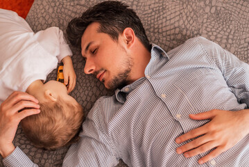 Wall Mural - A young father shares love with his son and spends time together at home, lying and sleeping on the bed, top view. 