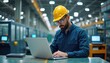 © Maryna - Engineer in factory reviews production data on laptop. Wears safety helmet, sits at table in modern factory. Industrial machines blurred in background. Scene shows tech worker analyzing production