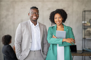Leinwandbilder - A diverse group of professionals engages in teamwork within a contemporary office environment. Two smiling leaders stand confidently in the foreground, promoting cooperation and success.