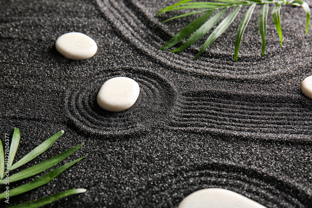 White stones and palm leaves on black sand with lines. Zen concept