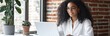 © k - Young woman with black curly hair working on laptop in bright modern office with potted plant