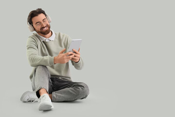 Handsome man in headphones with tablet computer sitting on light background