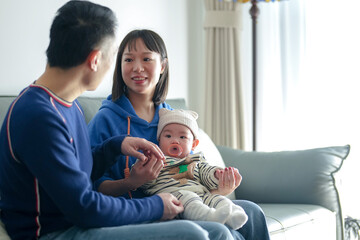 a 6-month-old boy spends time on a couch with his mother and father from a chinese family on a cold 