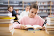 © JackF - Young girl sitting at table in reading room in library and doing homework.