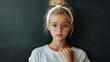 © Bargais - Sad young girl with glasses and a white headband standing against a blackboard.