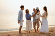© Take Production - family, party, sharing, parents, community, father, elder, loving, partnership, dad. A family of four, including a young girl, are standing on a beach. Scene is warm and family-oriented.