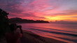 © Zape - A person taking a photo of a beautiful sunset over a calm ocean, with the sky painted in pink, purple, and orange hues. Capturing sunset over ocean.