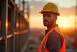 © Vibudhaart - Construction worker in yellow hardhat looking over shoulder at sunset.