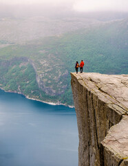 two individuals stand on the edge of preikestolen, a dramatic cliff in norway, gazing out at the vas