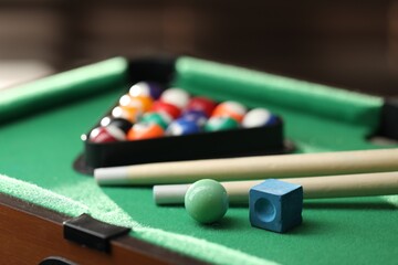 Wall Mural - Many colorful billiard balls in triangle rack, cues and chalk on green table indoors, closeup