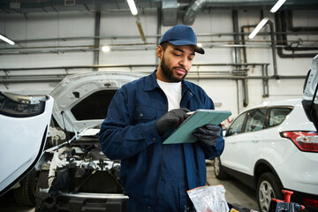 Handsome mechanic inspects vehicle information while working in a bustling auto repair shop