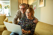 © Marko Geber - Senior couple online shopping on laptop on the couch at home