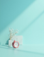 Poster - A small red alarm clock sits against a soft blue pastel colored background with gentle morning light nearby._00002_