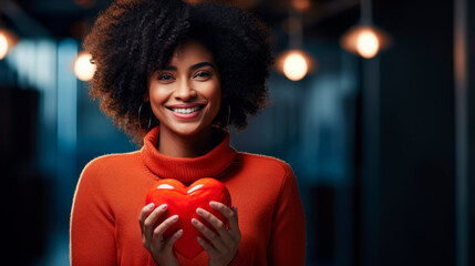 Wall Mural - Cheerful black woman with natural curls holds red heart portrait image. African american female in orange sweater picture photorealistic photography. Heartfelt concept photo realistic