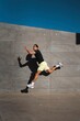 © Studio Marmellata - A man wearing yellow shorts and a black shirt leaps dynamically in the air, casting a shadow on a gray concrete wall under a bright blue sky