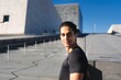 © Studio Marmellata - A man in a black shirt stands confidently outdoors with a modern architectural backdrop under a bright blue sky