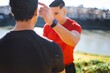 © Studio Marmellata - Two men share a powerful coaching moment with gestures and confidence, standing near a riverside surrounded by green and golden tones under bright sunlight