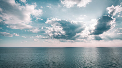 Wall Mural - Vast Calm Blue Ocean with Dramatic Sky, Fluffy White Clouds and Sunlight Rays Illuminating Water, Horizon Faintly Visible, Serene