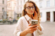 © maxbelchenko - Happy woman using phone walking in city street. Communication, social networks, blogging, online shopping concept.