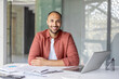 © Liubomir - Confident man sitting at desk with documents and a laptop, showcasing a professional setting. Ideal for work-related, business, and career concepts conveying positivity and productivity.