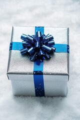 Wall Mural - vertical photo of a large silver Christmas gift box with a blue ribbon on a snowy white background bright lighting adding a touch of elegance