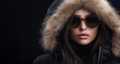 © GS Edwards Studio - A fashionable woman in sunglasses and a black winter coat on a black background, copy space