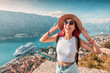 © EdNurg - Female tourist with backpack and hat enjoying the view of Kotor bay with cruise ship from fortress