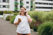 © mdyn - Happy young caucasian woman in good mood listening to music with headphones and standing on the street in the city. Music lover enjoying music. Urban lifestyle concept.