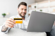 © Prostock-studio - Online banking concept. Happy millennial man with laptop and credit card sitting on sofa, selective focus. Positive guy enjoying making payments from home