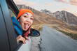 © EdNurg - Carefree tourist enjoying road trip, sticking tongue out of car window in mountain landscape