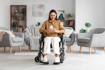 Wall Mural - Young woman in wheelchair using mobile phone at home