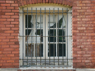 Isolated Close up Old red brick wall with white wood window. Black Steel security bars over the entire window. Torn curtain.  
