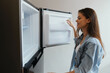 © SHOTPRIME STUDIO - Young woman in casual attire happily exploring her refrigerator, showcasing healthy food choices and a positive lifestyle, bright kitchen background