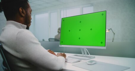 Wall Mural - Professional African American financial expert or marketing specialist enters data on computer with green screen chromakey. Mock up template for screen content. Modern office of E-commerce company.