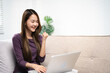 © Fahng - Young asian woman in good spirits working on laptop at home while sitting on couch. Excited female using computer notebook, happy celebrating success,receiving great news on notebook..