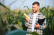 © Serhii - Yong handsome agronomist in the corn field and examining crops before harvesting. Agribusiness concept. agricultural engineer standing in a corn field
