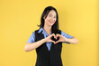 © Ika Rahma - Attractive Young Asian Woman Feels Happy and Romantic Shapes Heart Gesture on Yellow Background