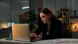 © kinomaster - Young business woman sits at desk works late night in office, using laptop, typing text on keyboard, angry frustrated expression, middle shot.