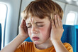 © Katerina Bond - Young child complaining of ear pain due to air pressure in an airplane, holding both hands to his ears and making a pained expression.