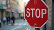 © Alex Pios - A close-up of a traffic sign indicating a stop, with a blurred urban background, highlighting the importance of road safety and compliance