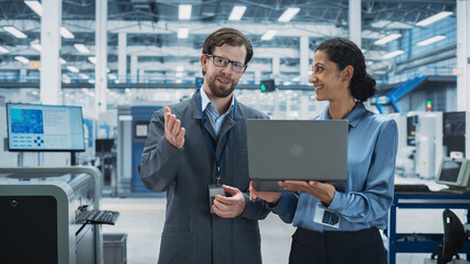 Leinwandbilder - Caucasian Man and Hispanic Female Having a Conversation at Industrial Facility. Advanced Factory Employees Working Together, Using Laptop Computer for Supervising Work Process At an Assembly Line.