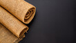 © Butsarakham - A rolled burlap fabric on a dark surface, showcasing its texture and natural color.