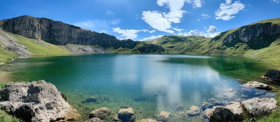 Aufkleber - Serene natural lake surrounded by lush green hills and rocky cliffs under a clear blue sky in a remote wilderness setting