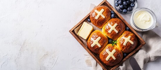 Poster - Delicious hot cross buns in a wooden tray with butter blueberries and cream on a textile napkin above a textured white concrete background