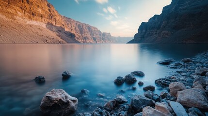 Aufkleber - Serene long exposure of tranquil lake at sunset with smooth water and rocky shoreline showcasing dusk colors and mountain reflections.
