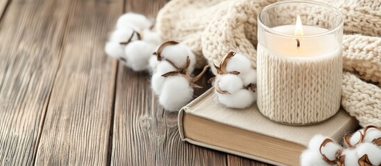 Poster - Cozy autumn arrangement with aromatic candle wool sweater cotton book on wooden background for a warm home vibe of comfort and relaxation