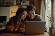 © TENphoto - Young couple enjoying a cozy evening together while watching something on a laptop in their warm living room