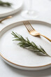© kazakova0684 - A modern minimalist table with a clean white theme, green sprigs on plates, and golden flatware